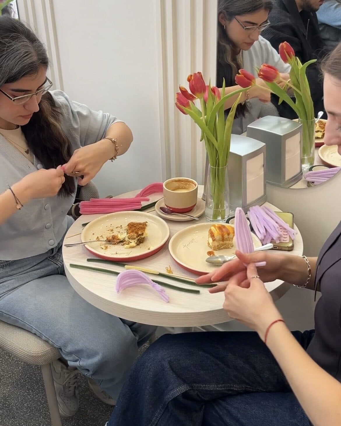 Participante la un workshop tougHER fac flori din sârmă colorată, la o masă cu cafea și lalele.